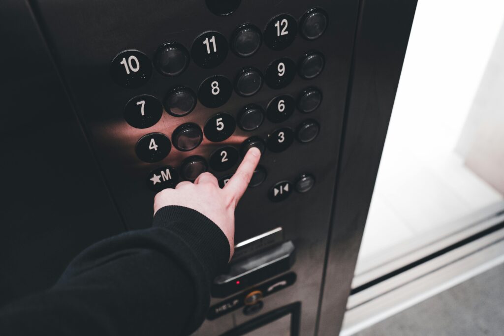 A person pressing the elevator button inside a modern elevator, showcasing the control panel with floor numbers.