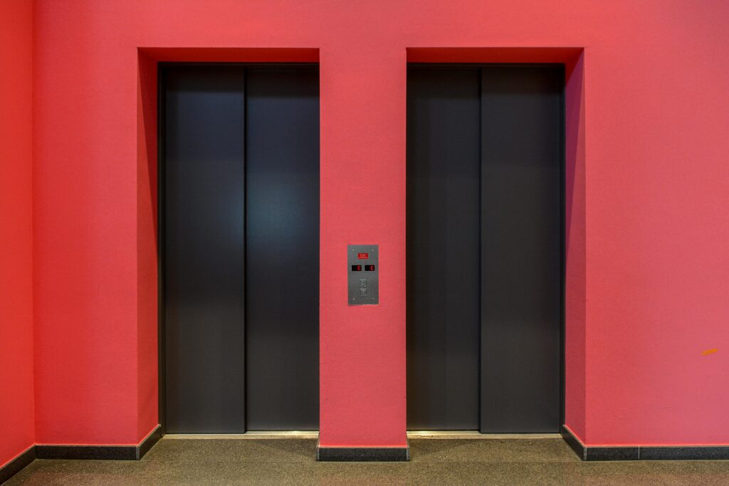 A pair of sleek modern elevator doors set against a vibrant red wall. Ideal for architectural themes.