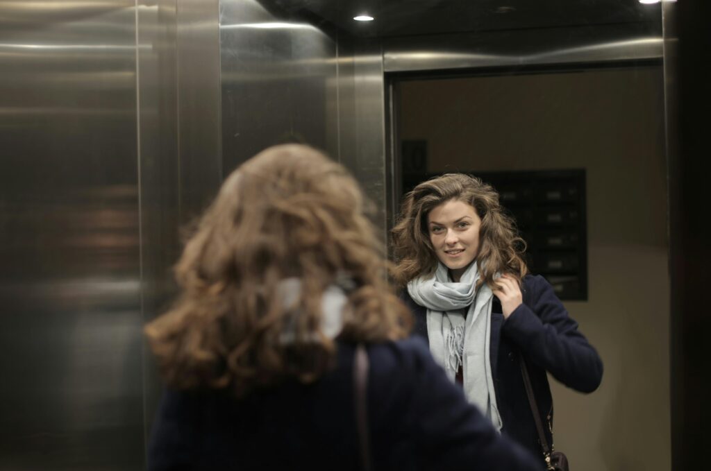 Stylish woman in an elevator admiring her reflection in the mirror while wearing a scarf.