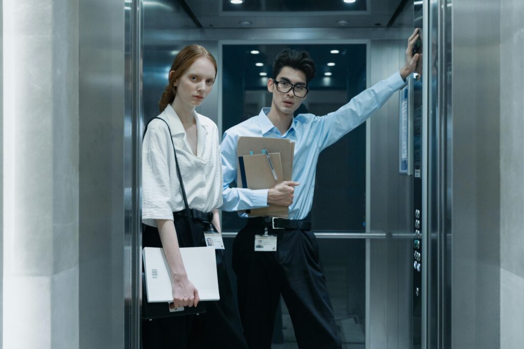 Two professionals in an elevator, standing with documents, in a corporate environment.
